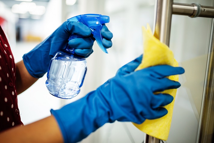 Closeup of woman's hands wearing blue rubber protective gloves spraying