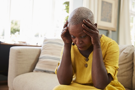 Senior woman sitting on sofa at home suffering from depression